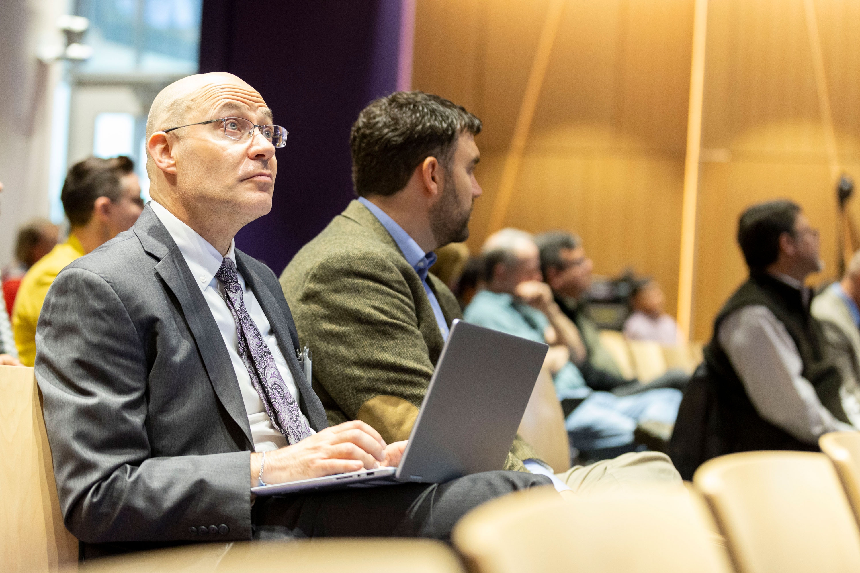 An R&E Week 2024 attendee sits in the audience, listening intently and taking notes on a laptop.