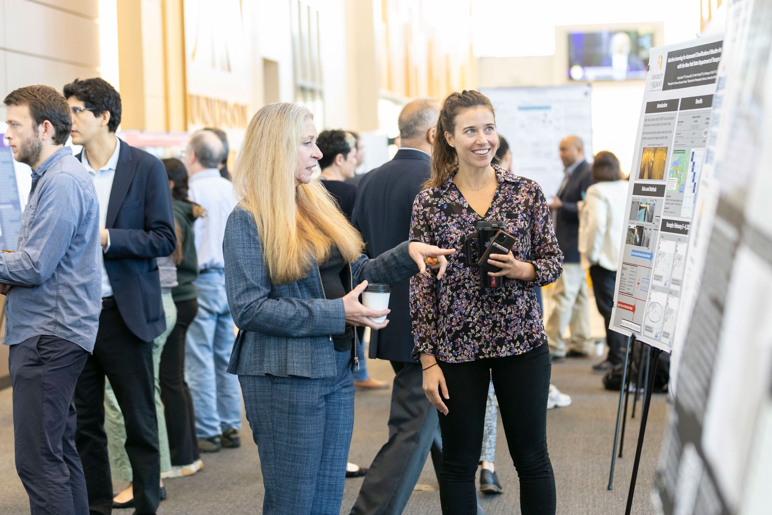 A researcher smiles as she speaks with an R&E Week attendee, who is gesturing toward her research poster.