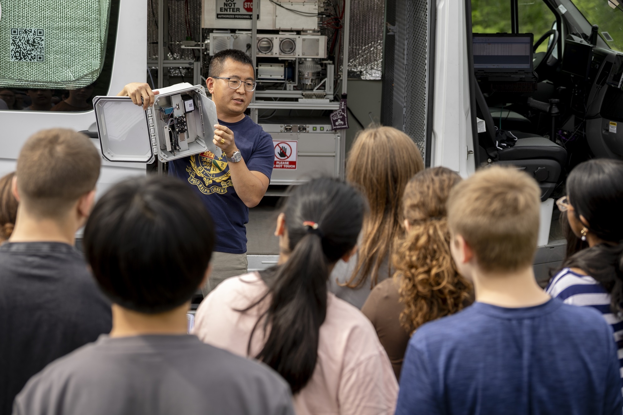 ASRC's Jie Zhang holds up instrumentation used in the mobile lab in front of Lisha Kill middle school students.