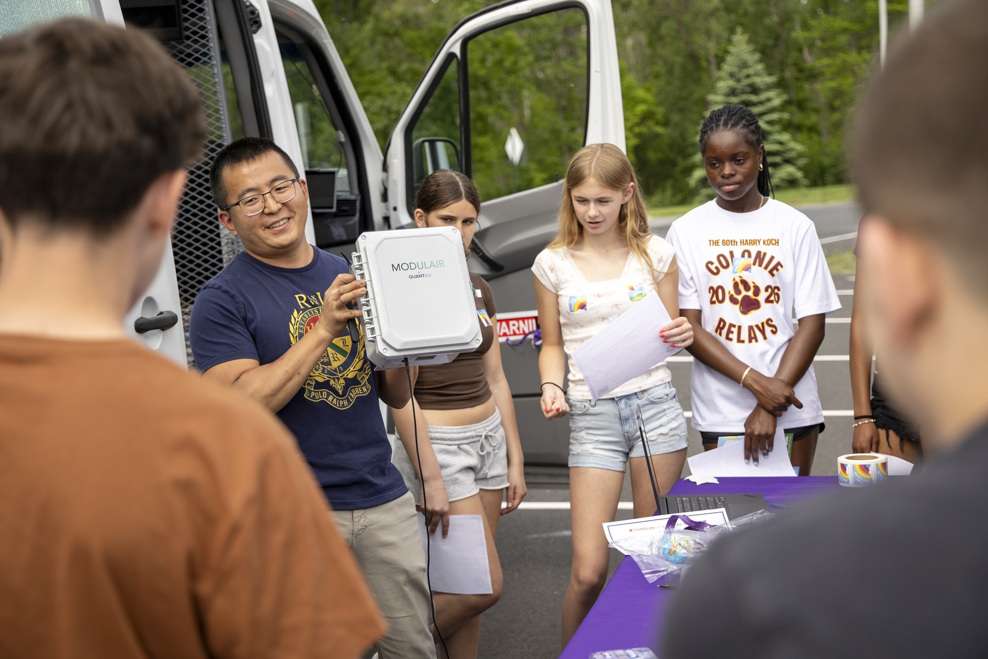 ASRC's Jie Zhang holds up instrumentation used in the mobile lab in front of Lisha Kill middle school students.