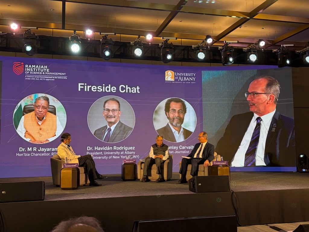 Three officials from UAlbany and RISM sit on stage and engage in a panel discussion. Behind them, a screen shows their names, titles and photos, as well as the words, "Fireside Chat."