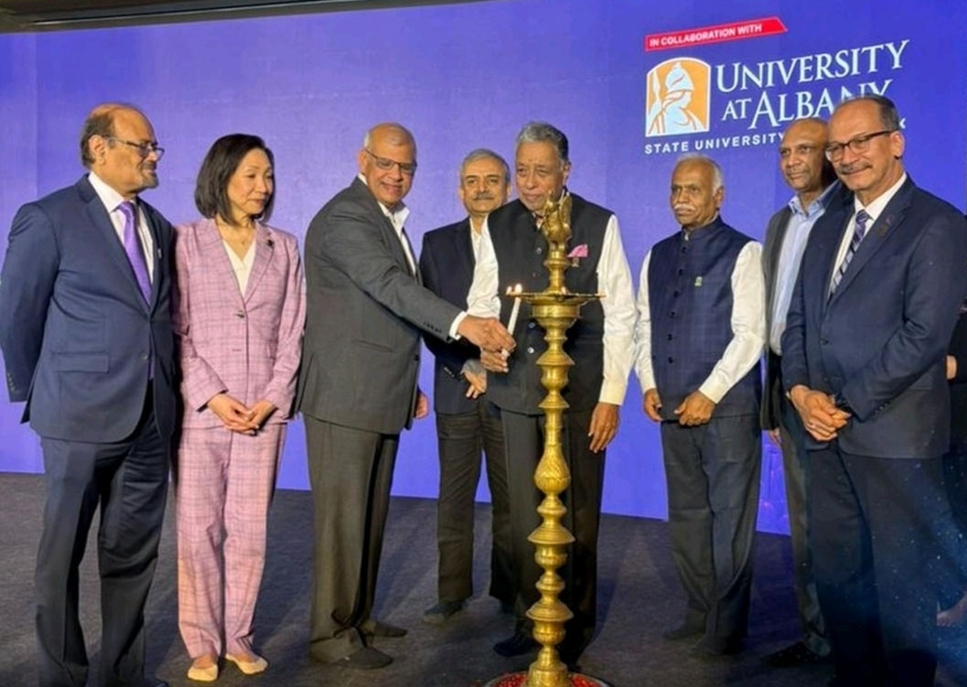 Eight officials from UAlbany and RISM stand together on stage as two use a small tapered candle to light a larger candle situated on a large gold candlestick.
