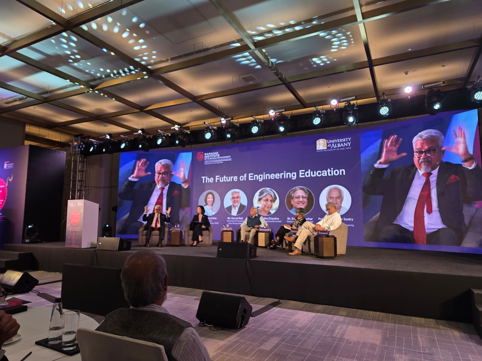 Five officials from UAlbany and RISM sit on stage and engage in a panel discussion. Behind them, a screen shows their names, titles and photos, as well as the words, "The Future of Engineering Education."