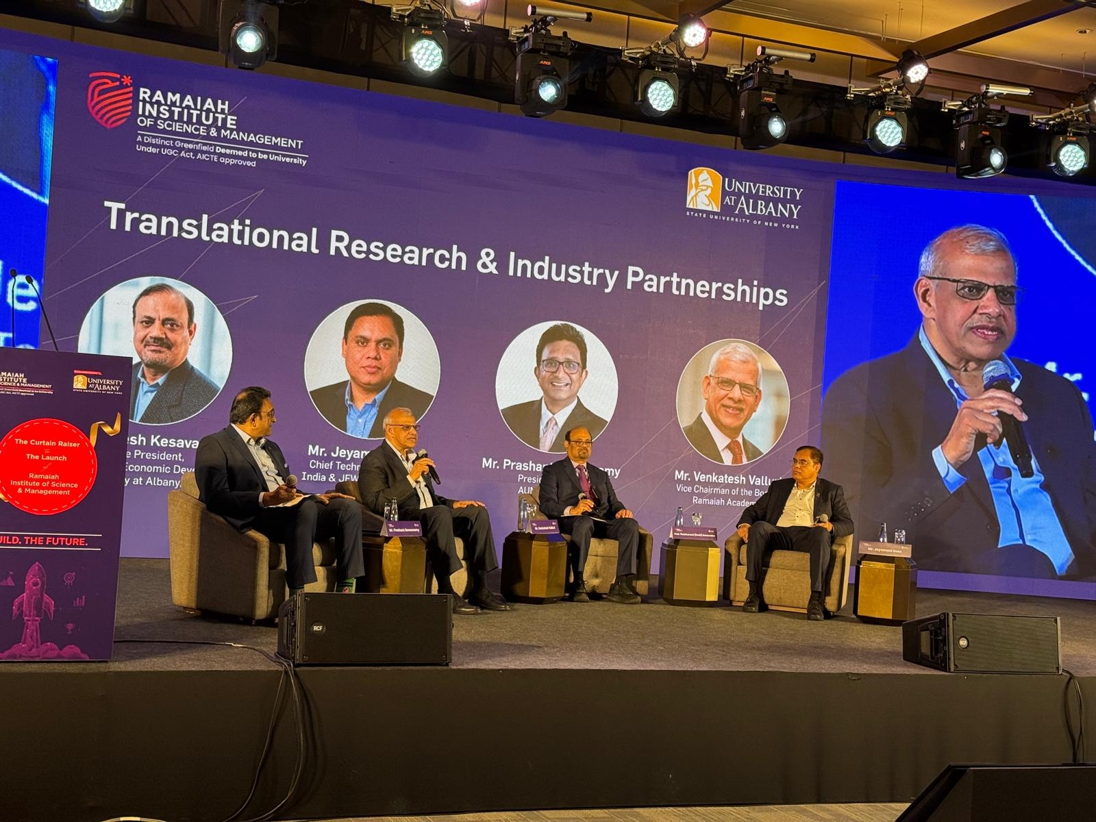 Four officials from UAlbany and RISM sit on stage and engage in a panel discussion. Behind them, a screen shows their names, titles and photos, as well as the words, "Translational Research & Industry Partnership."