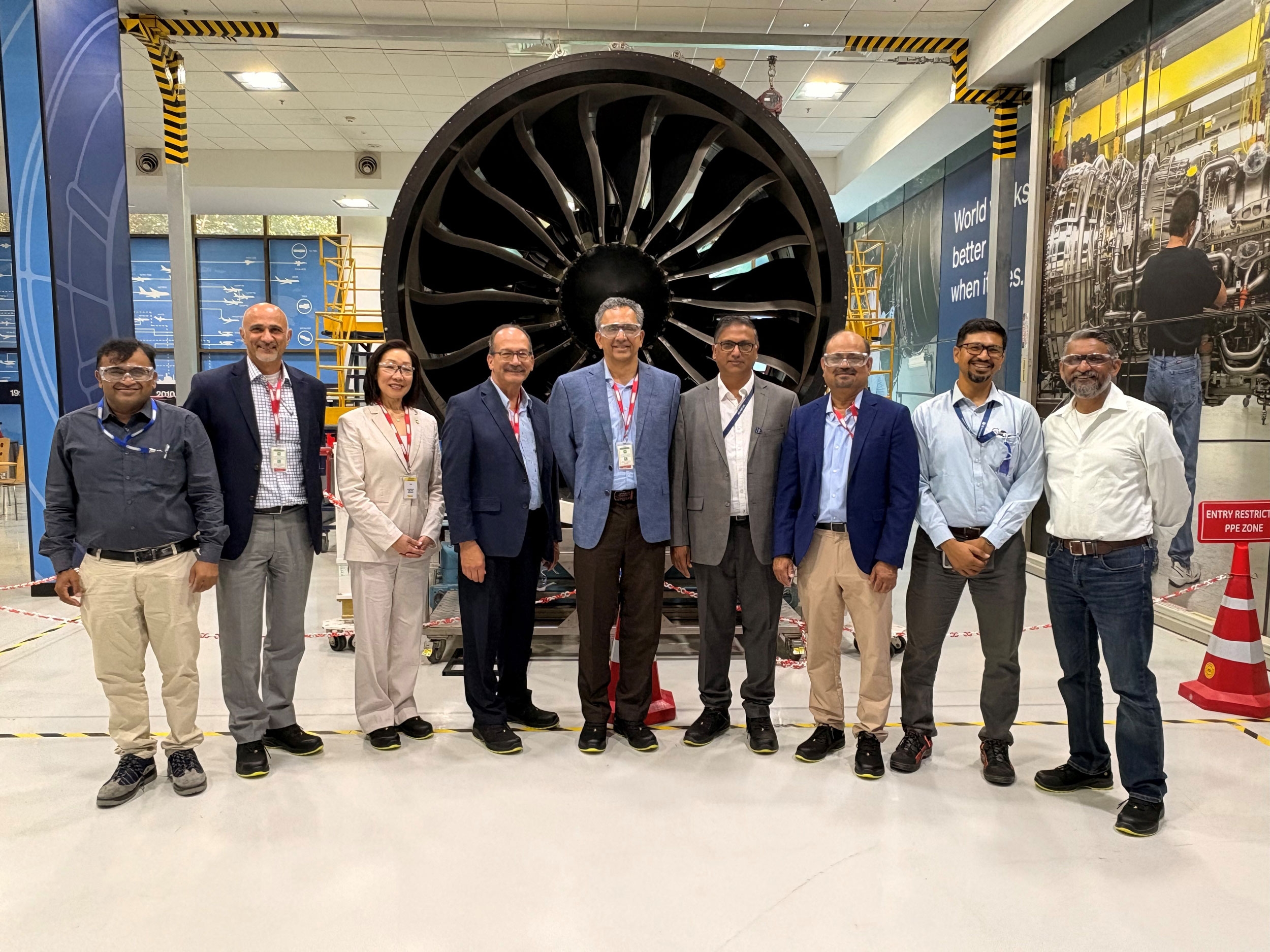 Eight officials from UAlbany and RISM pose for a photo inside an aerospace research and development facility.