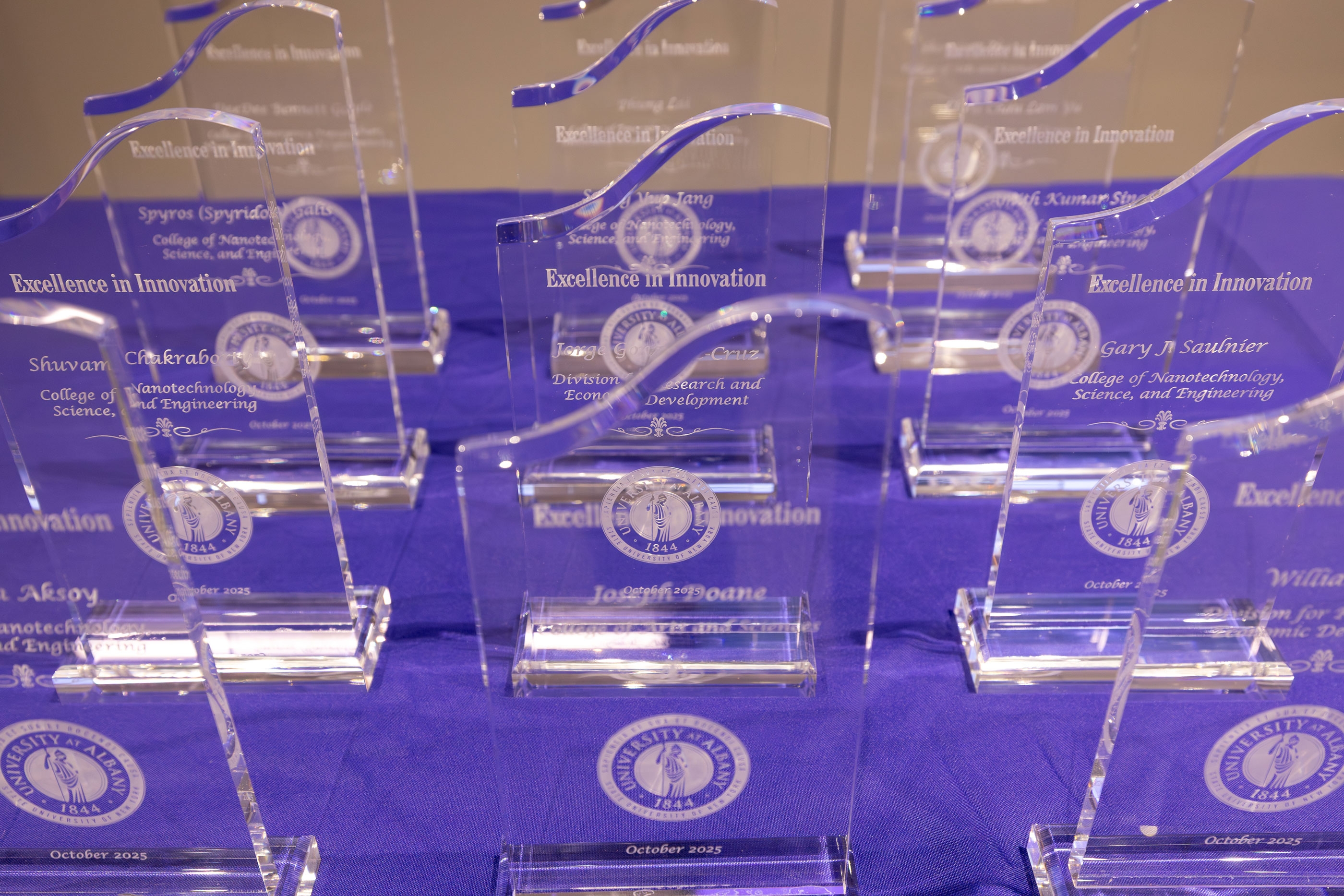 A dozen glass Excellence in Innovation awards are arranged in neat rows on a table with a purple tablecloth.