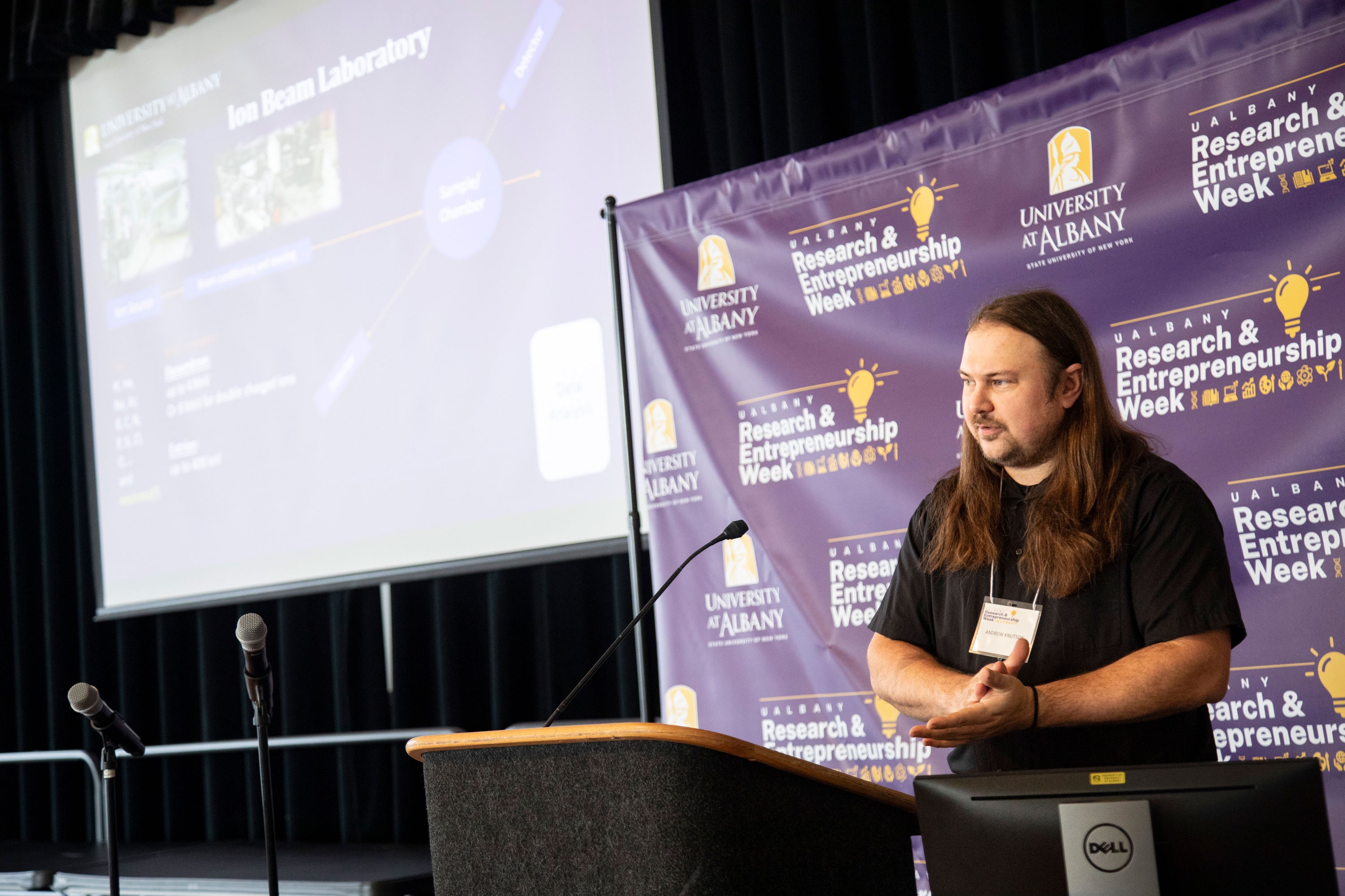 A researcher stands at a podium and speaks about the Ion Beam Laboratory during R&E Week 2023.
