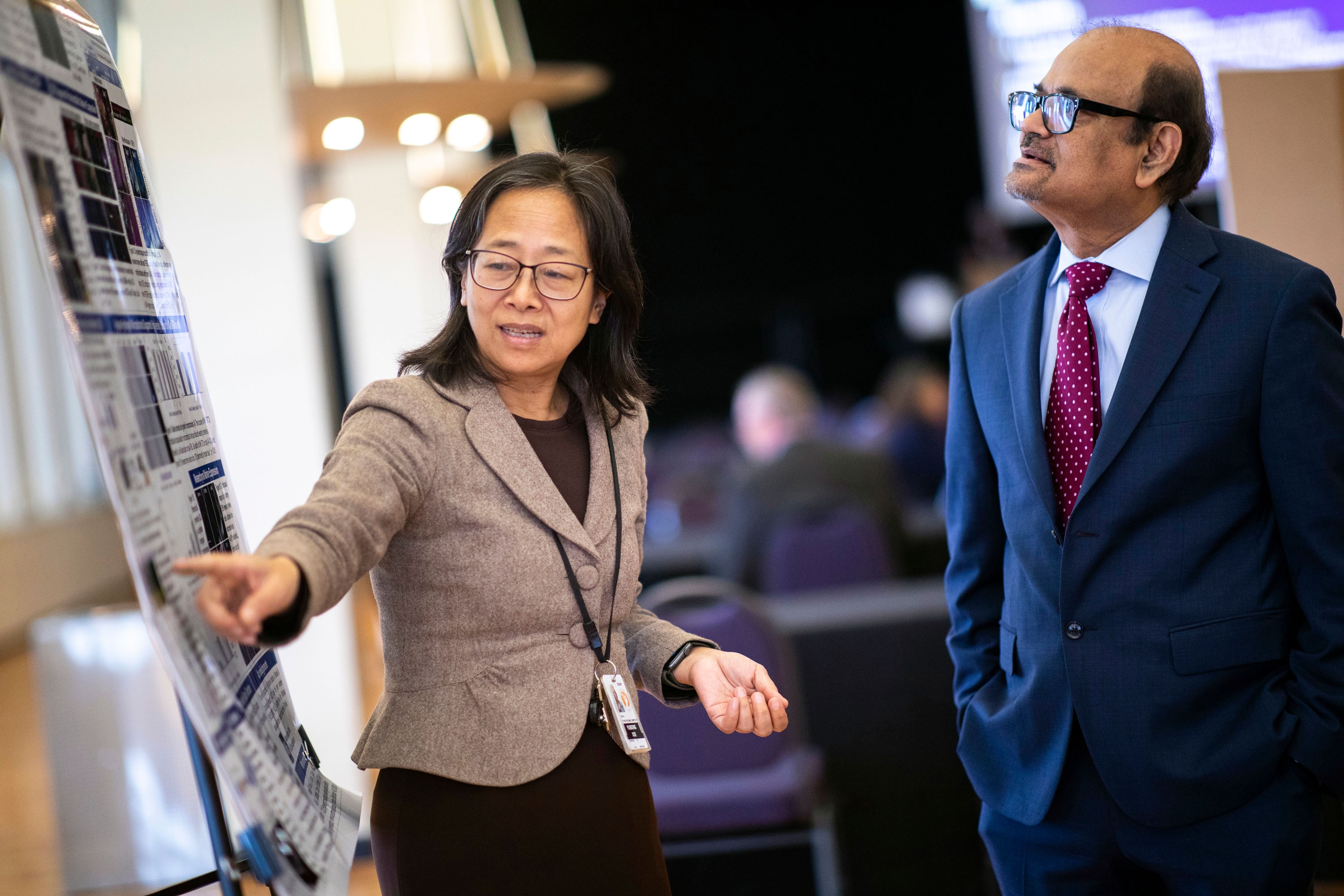 A faculty member points to her research poster while conversing with UAlbany Vice President for Research & Economic Development Thenkurussi (Kesh) Kesavadas.
