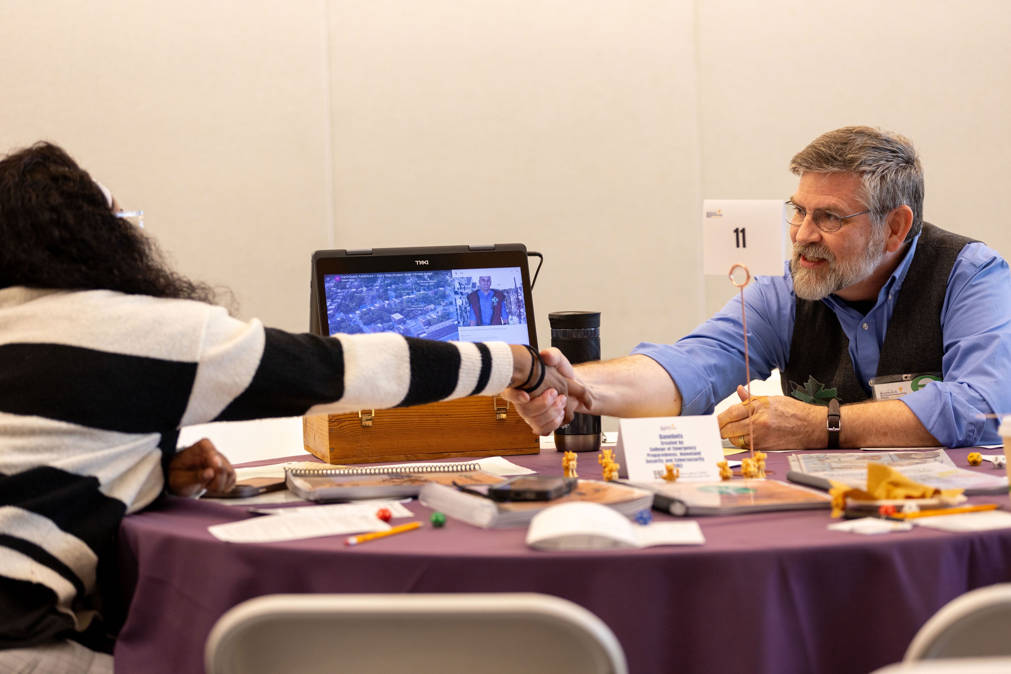 A researcher and a student seated at a table shake hands during a RISE pitch session.