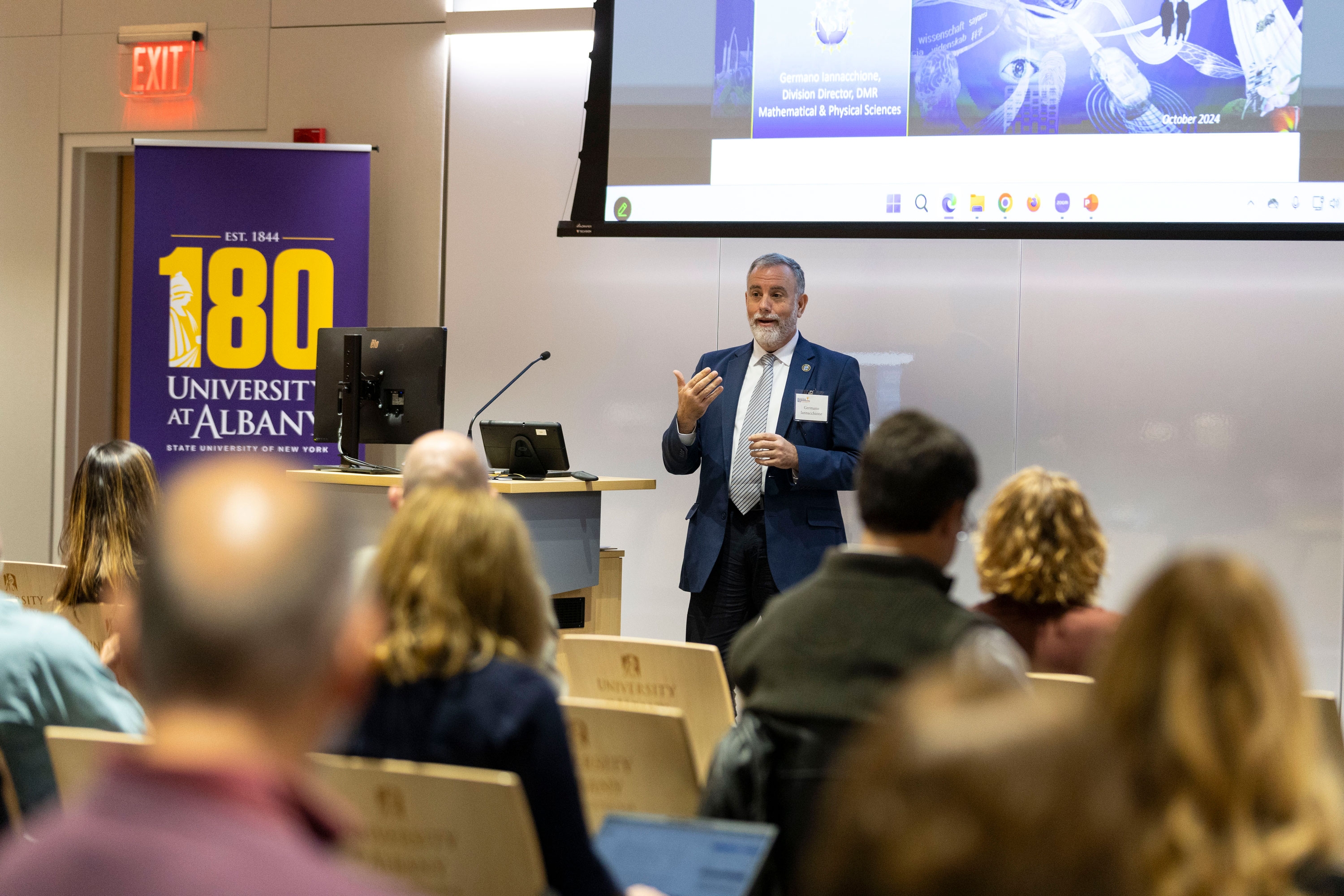 A presenter gestures while speaking in front of a seated group of R&E Week 2024 attendees.