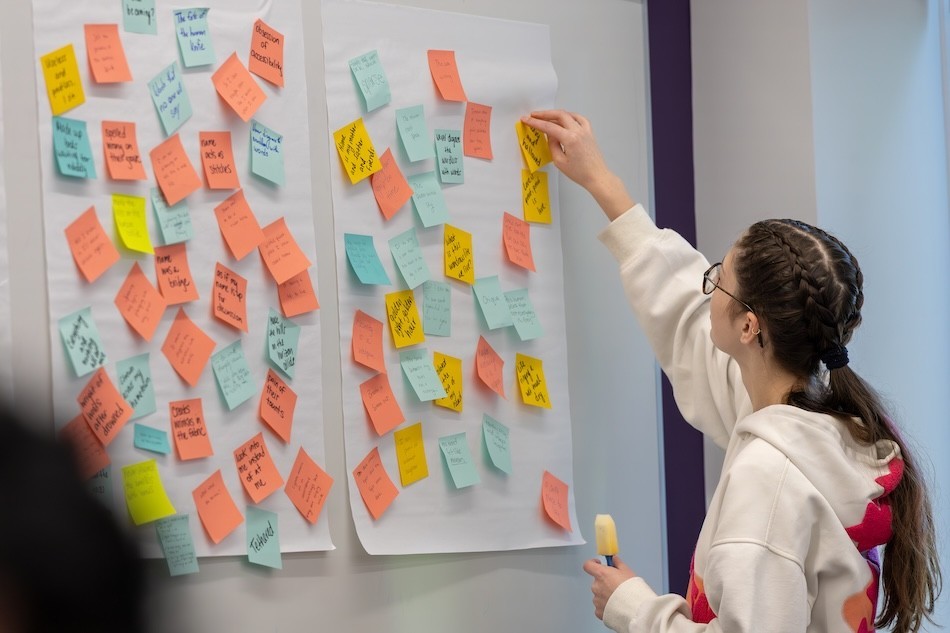 A teen girl hands a post-it note on a wall of colorful post-it notes