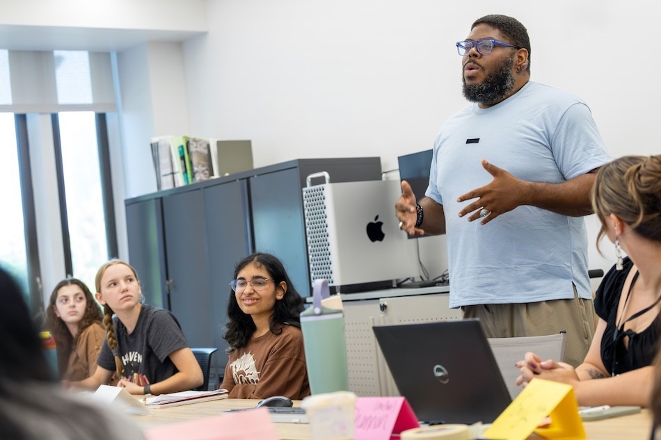 A man gestures and speaks in front of a classroom of teen writers