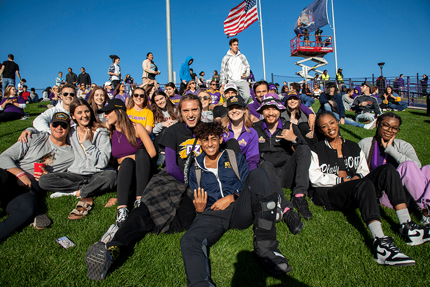 A large group of students sit on the grass, posing and smiling for a photo.