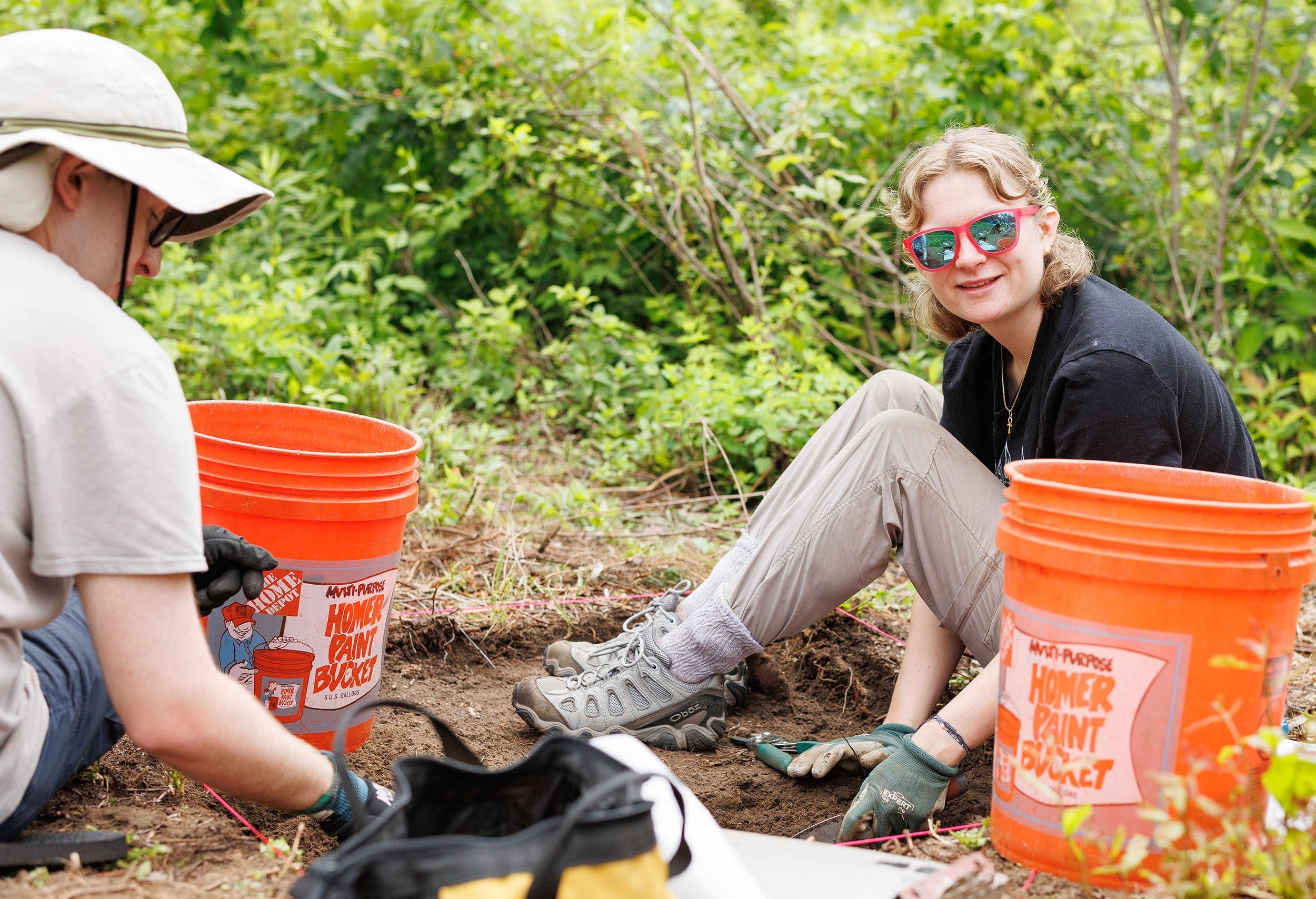 A young woman sits in a dirt grid a field school and smiles as she looks at the camera in Albany's Pine Bush.