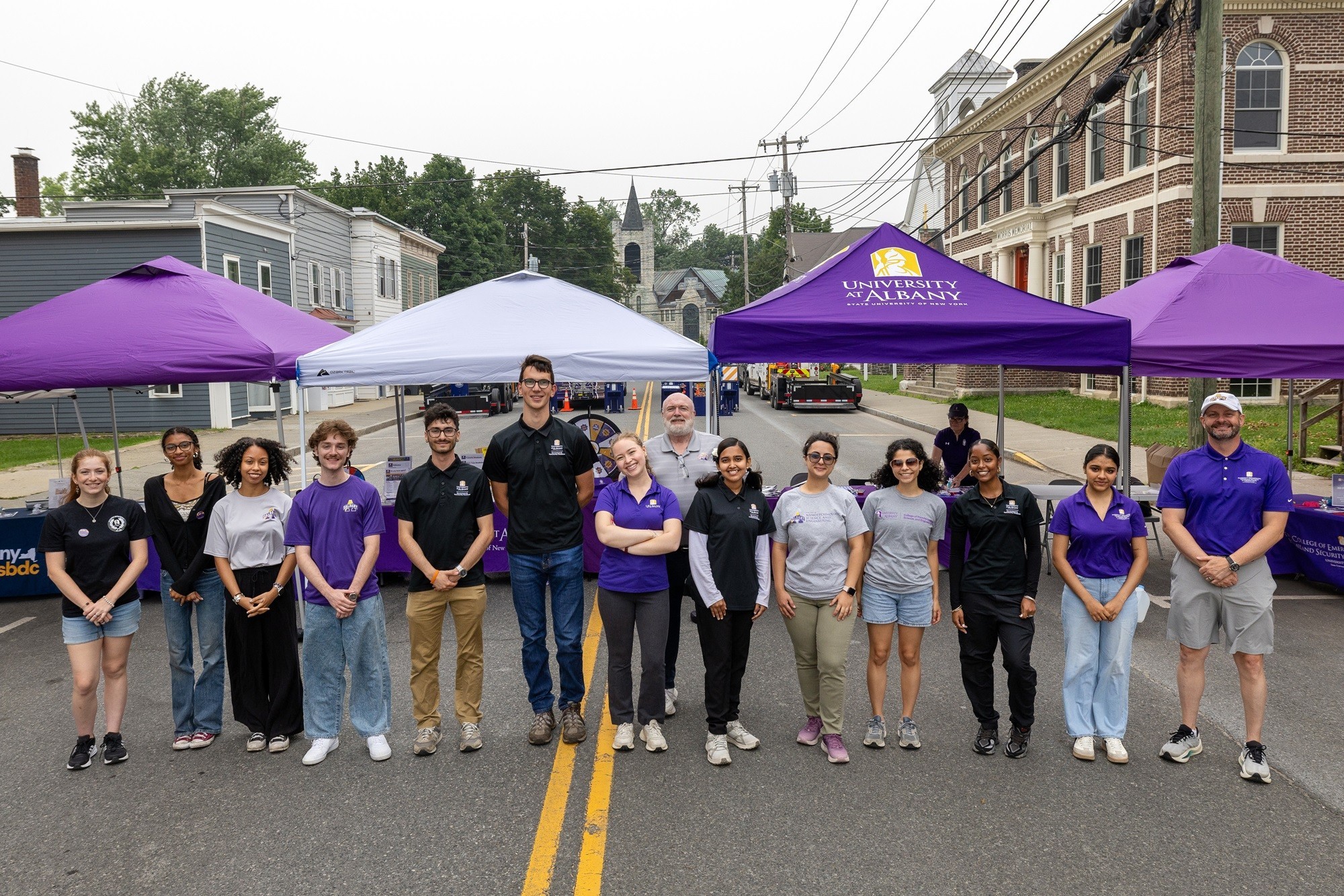 Group stands in front of purple and white pop up tents.