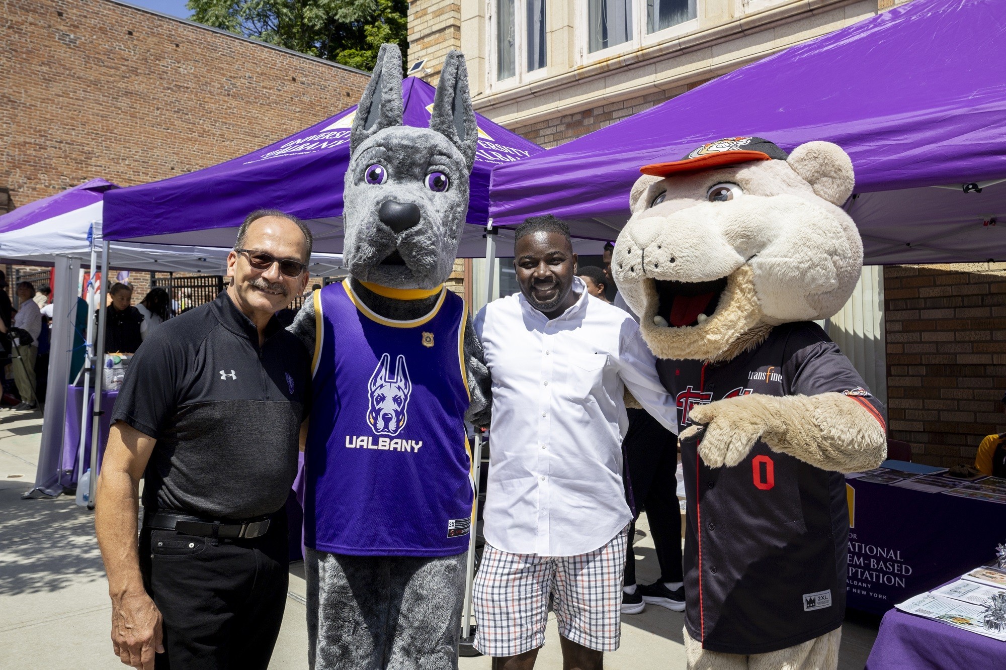 Two men and two mascots pose for a picture at an event.