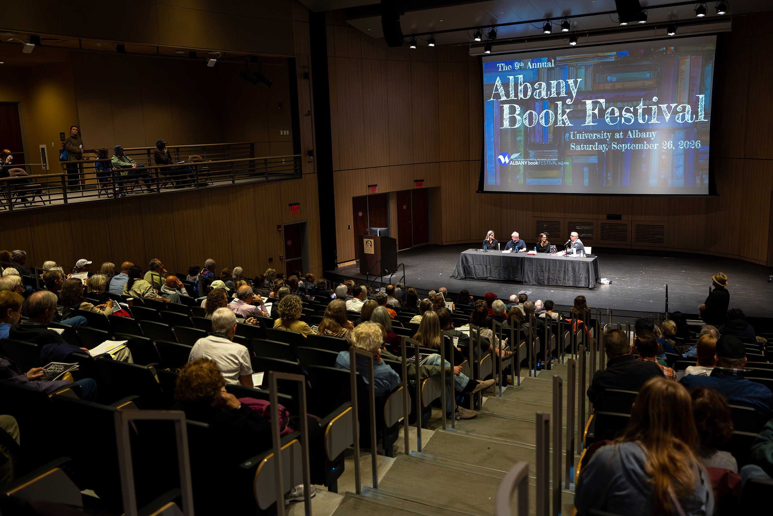 An interior of a large auditorium from the seats looking toward a stage with a table and several people seated at it.