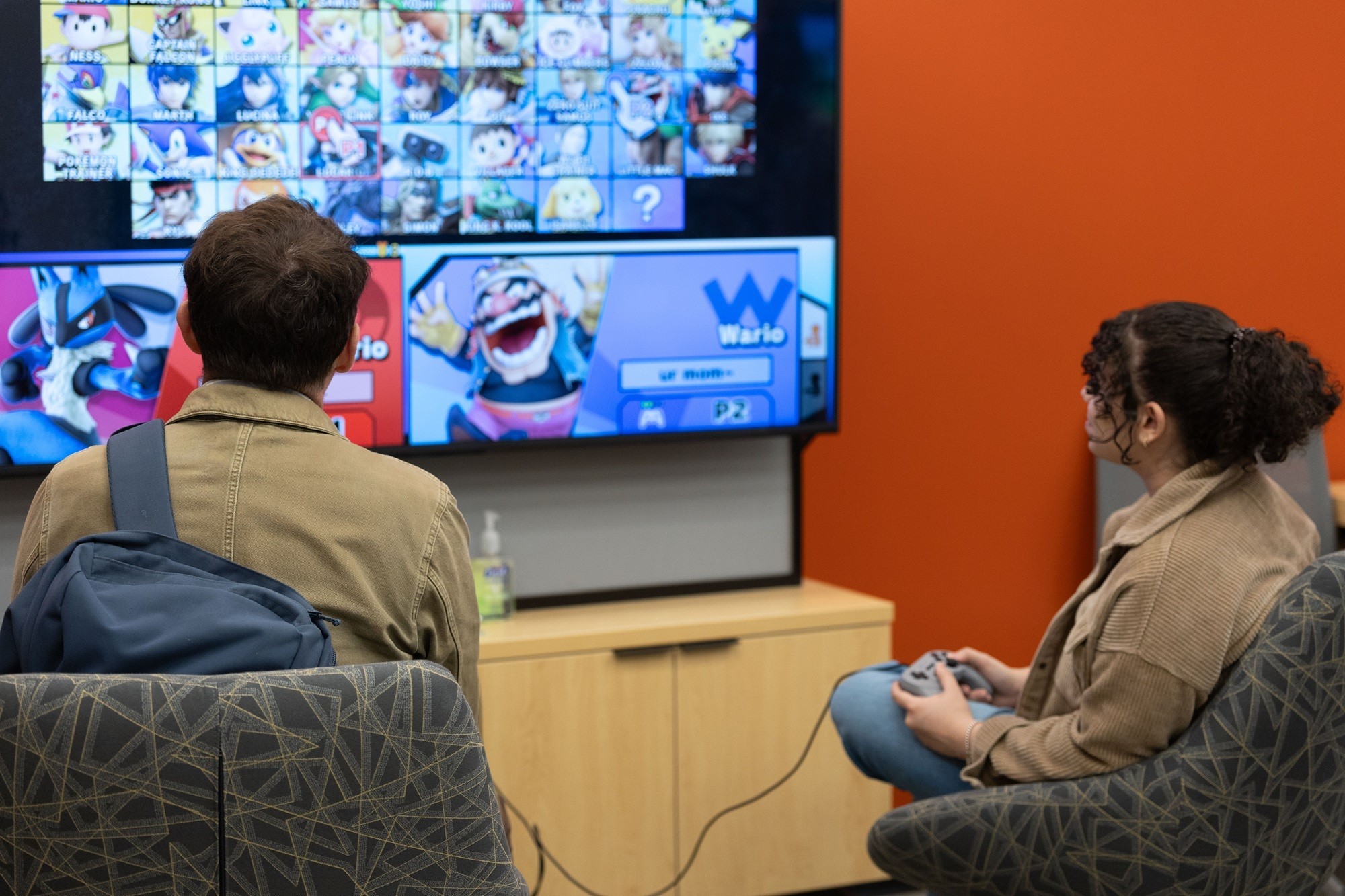 A professor and student compete in a Nintendo game inside the Game Hub.