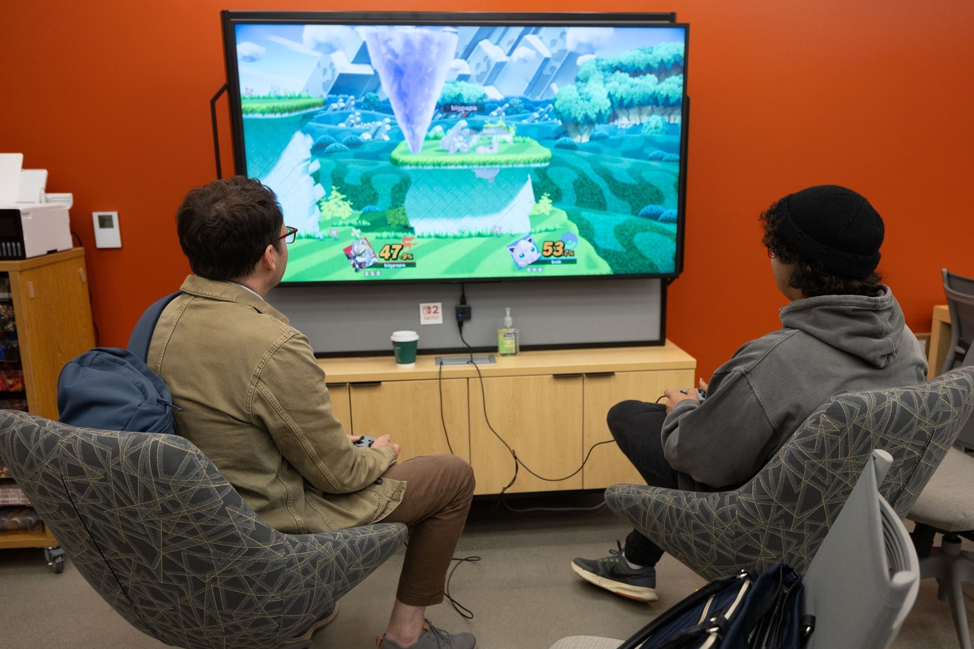 A professor and student compete in a Nintendo game inside the Game Hub.