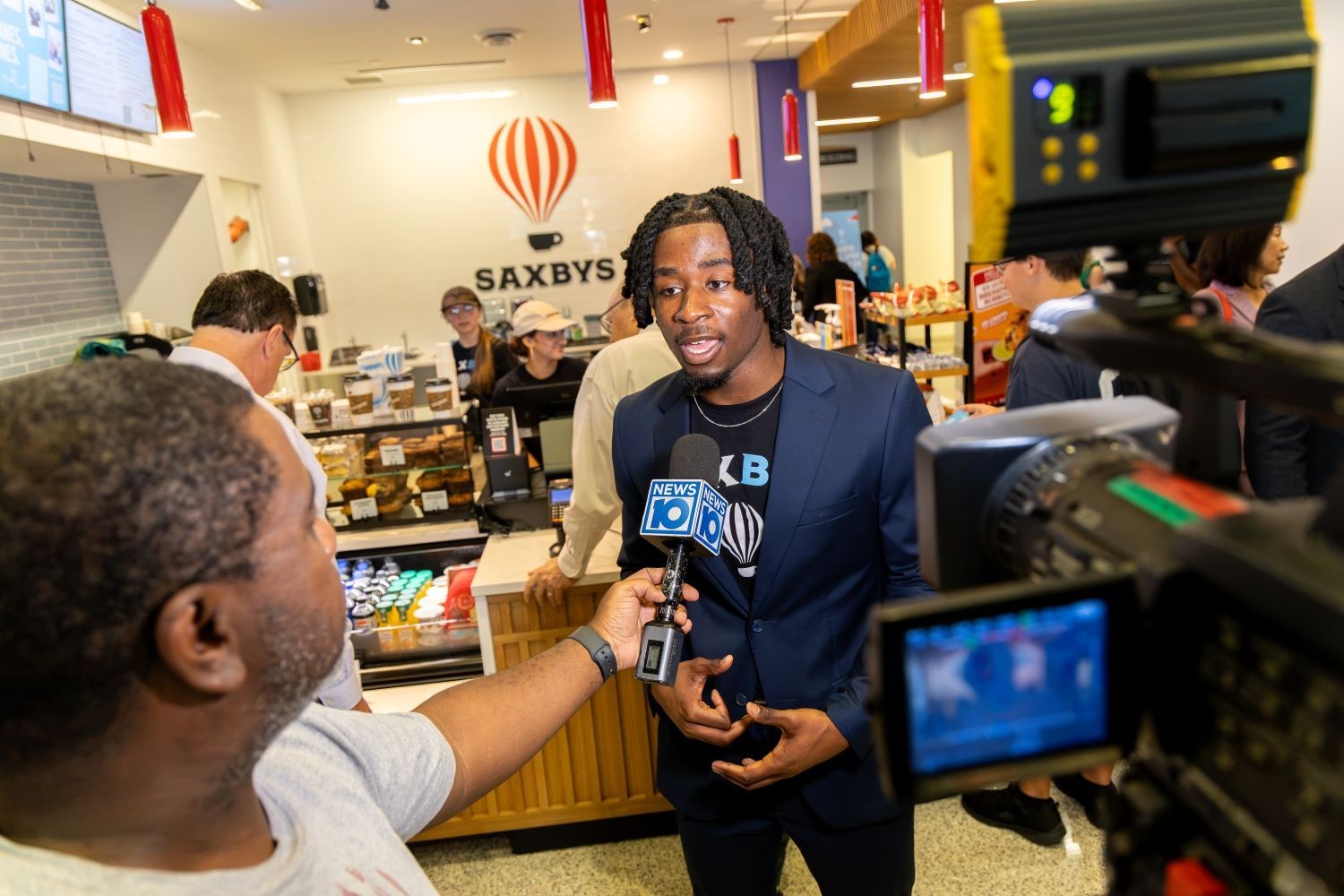 The student CEO of Saxbys inside the Massry School of Business Theo Rhynie is interviewed by a TV station 