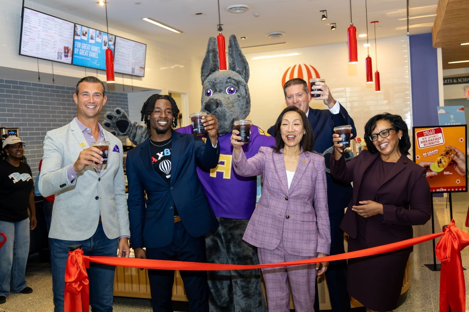 A group of people stand in front of a ribbon cutting with iced coffee in their hands during the opening of a new Saxbys cafe inside the Massry School of Business at UAlbany