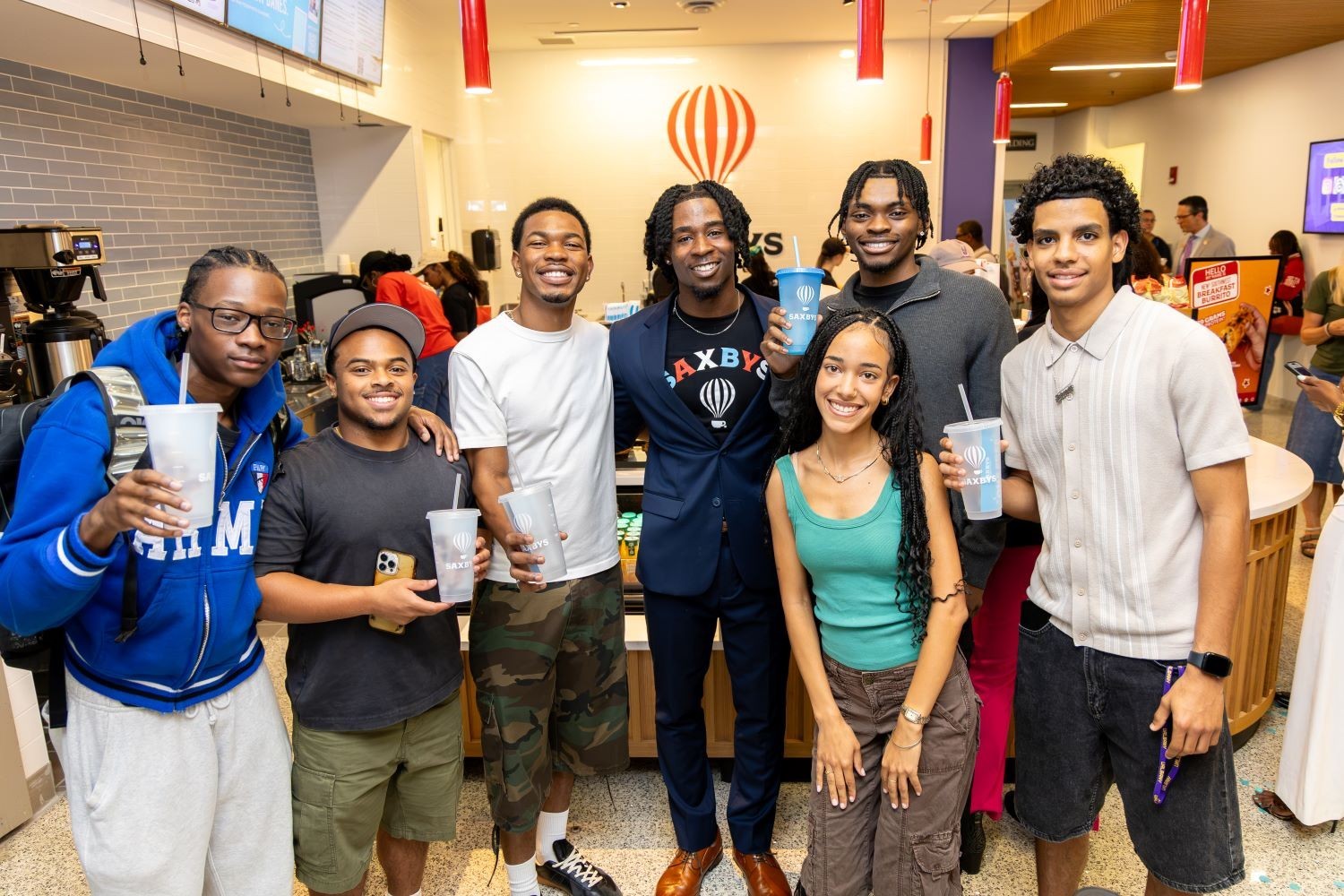 A large group of students stands in front of the new Saxbys cafe inside the Massry School of Business