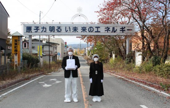 Yuji Onuma and his wife, Serina hold the ashes of his aunt in front of a sign in Fukushima that reads "Atomic power: Energy for a bright future."