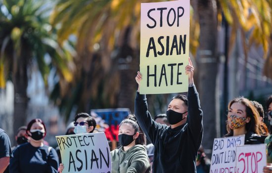 A young man holds up a Stop Asian Hate sign amidst a crowd of people holding similar signs below his