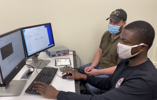 Two college students in facemasks work together on a computer