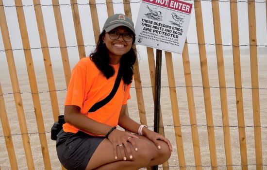 Student Mya Darsan crouches next to a fence affixed with a "Do Not Enter" sign, which explains that the bird nests and eggs in that area are a protected species.