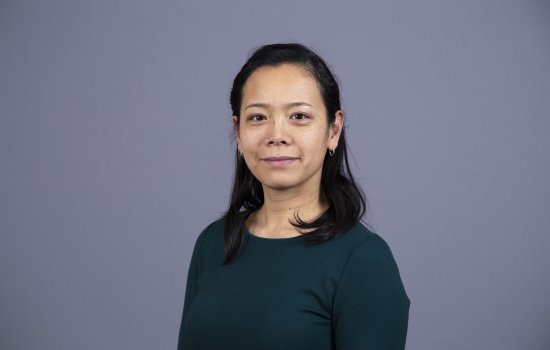 Tomoko Udo stands against a grey background and smiles at the camera.