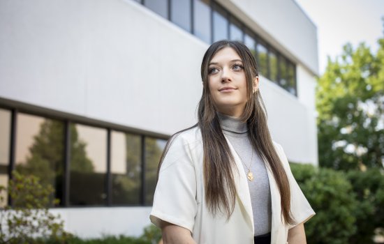 Student Cassie Kane stands in front of the School of Public Health, looking to the side.