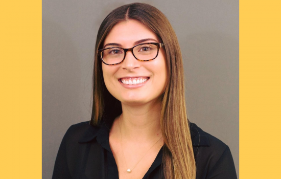 Sebesta shown smiling in a black shirt with glasses on, yellow border around photo.