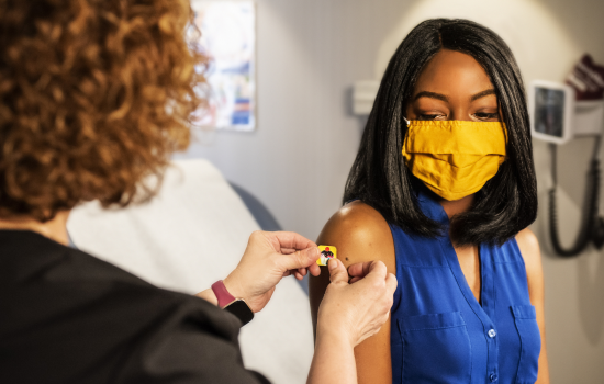 A woman wearing a yellow face mask receives a flu shot.