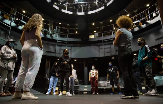 Students in a circle look up in a black arena theater