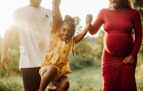 A young girl wearing a yellow dress is swinging in between her mother and father.