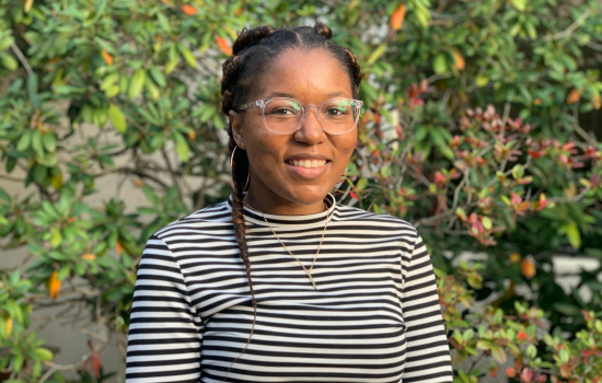 Jabrea Robinson smiles at the camera, outside the School of Public Health. Behind her are green bushes.
