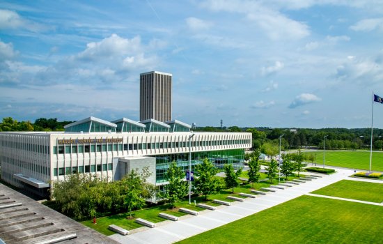 a modern cement and glass building with a row of trees and a green lawn