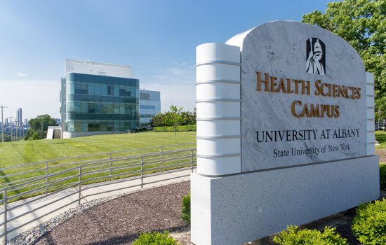 An exterior shot of the Health Sciences campus on a sunny day, with the "Health Sciences Campus" sign in the foreground and the Cancer Research Center in the background.