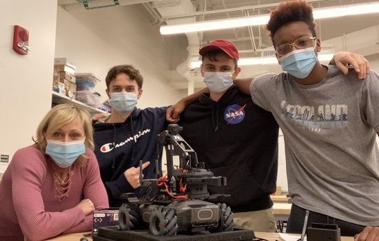 Marcie Fraser and three students in the EPICH program stand in front of a robot inside CEHC's makerspace at ETEC. 