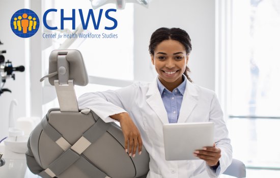 A female doctor leans against a dentistry chair and holds a tablet.