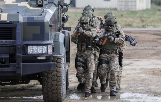 Ukraine military members armed with guns walk next to a transport vehicle on a muddy road during training in 2019.