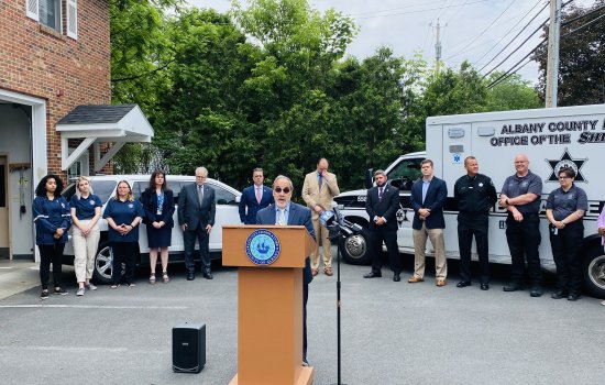 In the forefront, Carmen Morano, professor in School of Social Welfare, speaks at a podium during the press conference announcing ACCORD. Other program leaders stand in the background, in front of an ambulance.