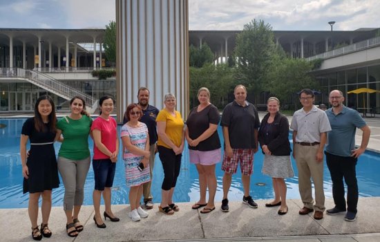 A group of 11 adult men and women stand in front of the main fountain pond.