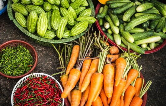 Produce vegetables sit in plastic baskets on a dirt floor.