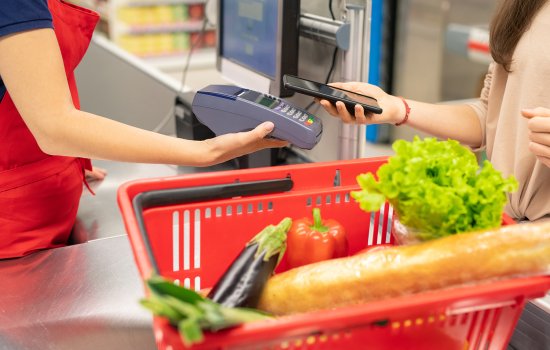 A woman pays for vegetables at a grocery store with her phone.