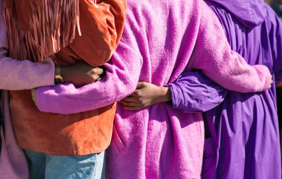 A group of diverse women embrace while standing outside.