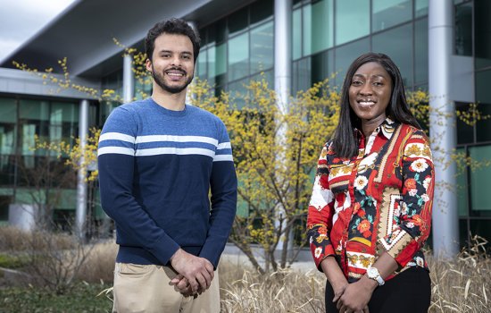 A young man and young woman stand beside each other, smiling, in the courtyard of the Life Sciences Research Building