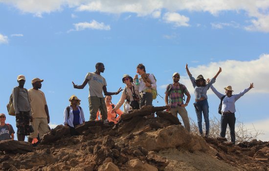 Students stand on a rocky hilltop and make celebratory poses.