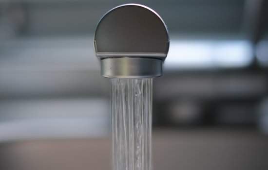 Water streams out from a silver kitchen faucet.